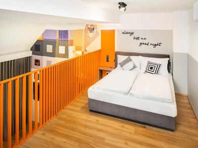 Chambre d'hôtel confortable avec lit double, rampe d'escalier orange et décoration murale moderne.