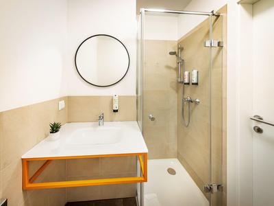 Salle de bain lumineuse avec douche en verre, lavabo rectangulaire et miroir rond au mur.