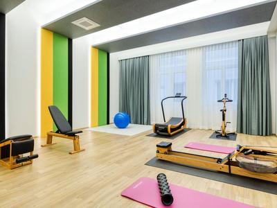 Salle de fitness lumineuse avec tapis de yoga, équipements d'exercice et grandes fenêtres avec rideaux.