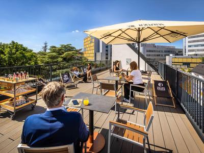 Terrasse sur le toit avec tables, chaises et parasols, des clients profitent du soleil.