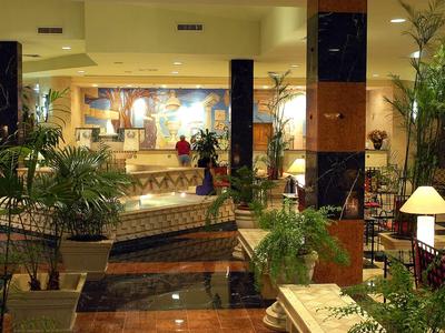 Große Hotellobby mit Marmorboden, Pflanzen, Polstermöbeln und dekorativen Lampen.