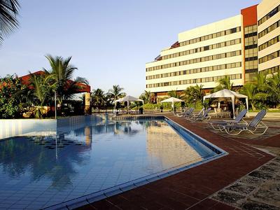 Großer Außenpool mit Liegestühlen vor einem modernen Hotelgebäude bei klarem Himmel.