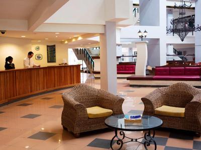 Helle Hotellobby mit Sitzbereich, hölzernem Empfangstresen und moderner Beleuchtung.