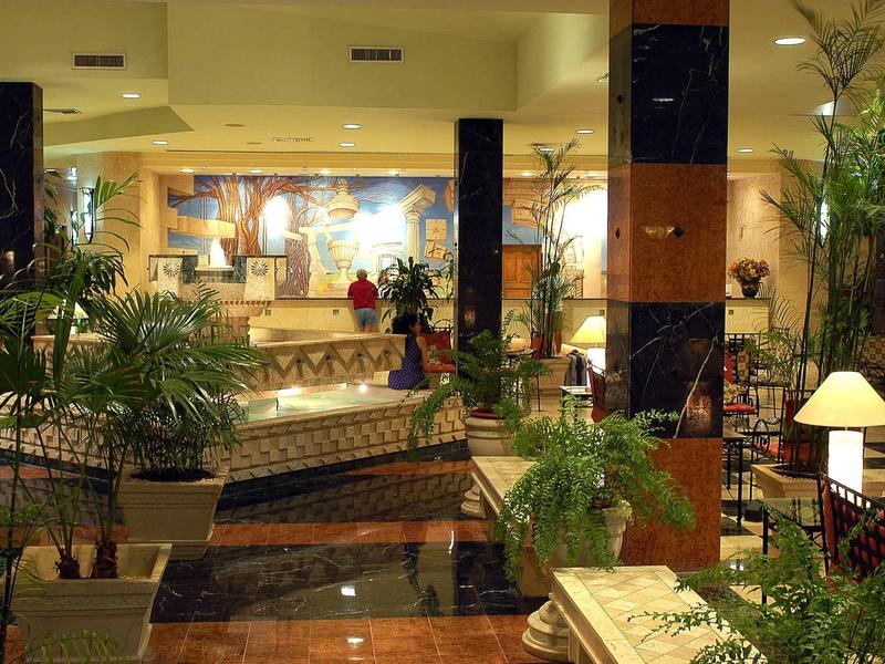 Große Hotellobby mit Marmorboden, Pflanzen, Polstermöbeln und dekorativen Lampen.