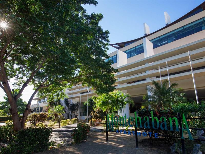 Modernes mehrstöckiges Gebäude mit blauer Fassade, Bäumen und Sonnenschein im Vordergrund.