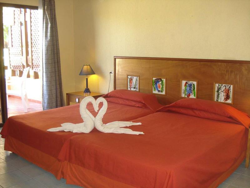 Zwei Betten mit roten Decken, zwei Handtücher in Form von Schwänen auf der Mitte, warme Beleuchtung.