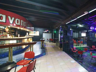 Moderner Barbereich mit roten Stühlen und einem beleuchteten Havana-Schild an der Wand.