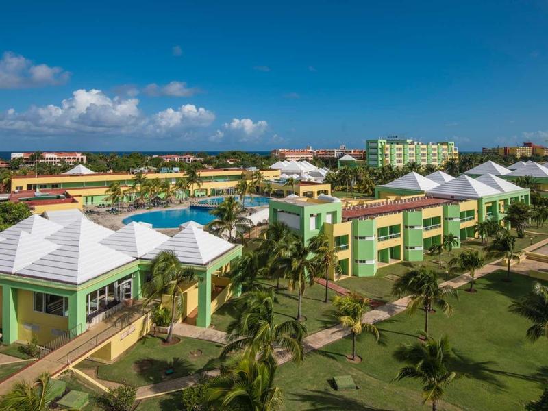 Bunte Gebäude mit weißen Dächern, umgeben von Palmen und einem klaren blauen Himmel.