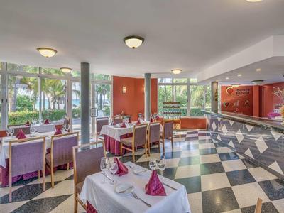 Helles Restaurant mit schwarz-weiß kariertem Boden, rot dekorierten Tischen und Fensterblick auf grüne Bäume.