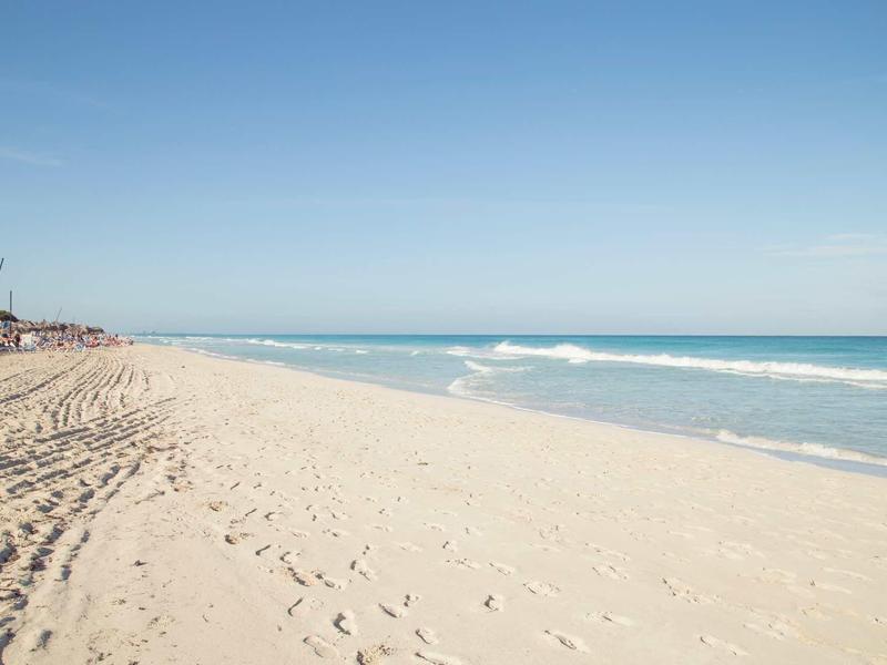 Breiter Sandstrand mit sanften Wellen und klarem blauem Himmel am Meer.