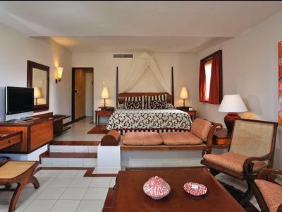 Helles Wohnzimmer mit braunen Möbeln, Sofa, Stühlen, TV und großem buntem Wandbild.