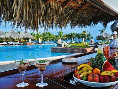 Bar am Pool mit tropischen Früchten, Cocktails und Palmen unter Sonnendach am blauen Wasser.