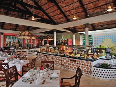 Großes Restaurant mit gedeckten Tischen, Holzstühlen und Buffetbereich unter einem Strohdach.