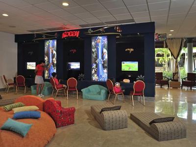 Großer Raum mit Sofas, Sitzkissen, Stühlen und digitalen Bildschirmen an schwarzen Trennwänden.