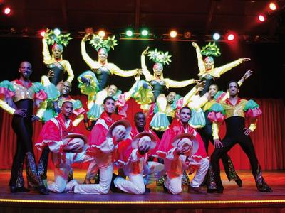 Bunte Tanzgruppe in auffälligen Kostümen posiert auf Bühne mit Lichtershow