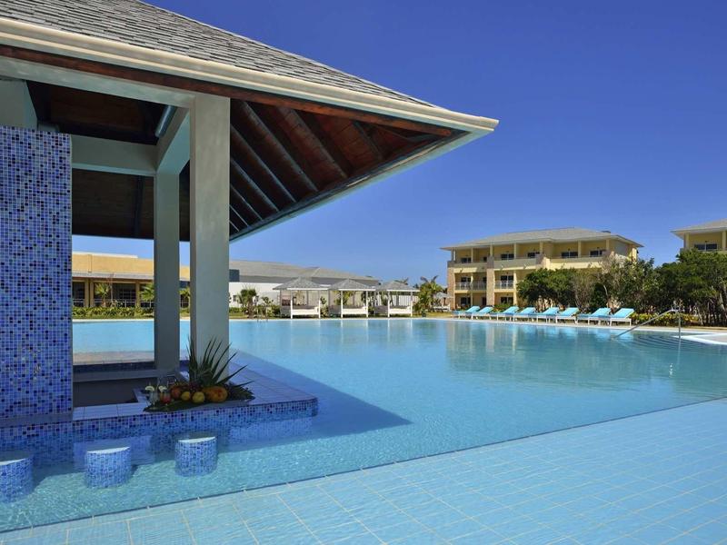 Großer Pool mit blauen Fliesen und umliegenden Hotels unter klarem Himmel.