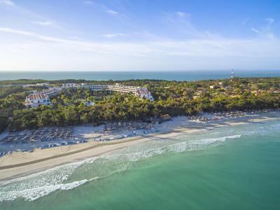 Überblick über einen Strand mit sanften Wellen, grüner Vegetation und Hotels im Hintergrund.