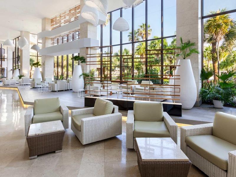 Helles, modernes Wohnzimmer mit großen Fensterfronten, weißen Sesseln und grünen Pflanzen.