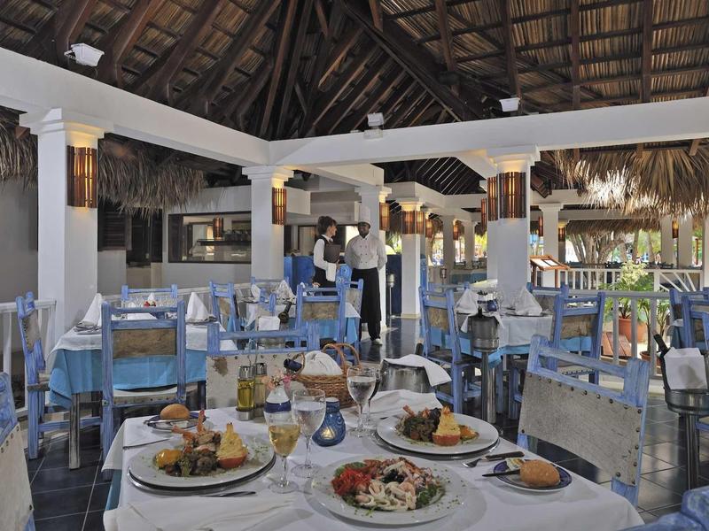 Restaurant mit gedeckten Tischen und Blick auf das Meer, rustikales Dach und entspannte Atmosphäre.