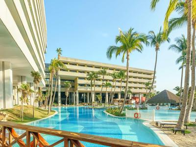 Moderner Hotelpool mit Palmen und Liegestühlen unter blauem Himmel.