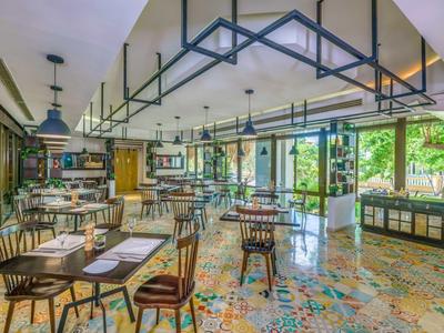 Helles Restaurant mit buntem Fliesenboden, Holztischen und großer Fensterfront zum Garten.