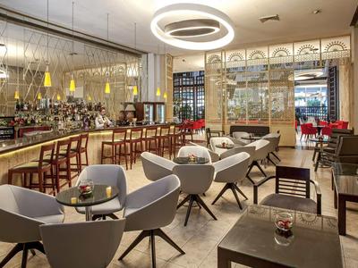 Moderner Restaurantraum mit grauen Sesseln, Holztischen, Bar und runden Deckenlampen.