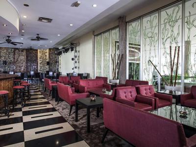 Moderne Bar mit schwarzen und weißen Fliesen, roten Sitzbänken und großen Fenstern mit Pflanzenmuster.