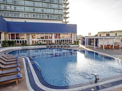 Moderner Außenpool mit Liegestühlen neben Hotelgebäuden bei Sonnenuntergang.