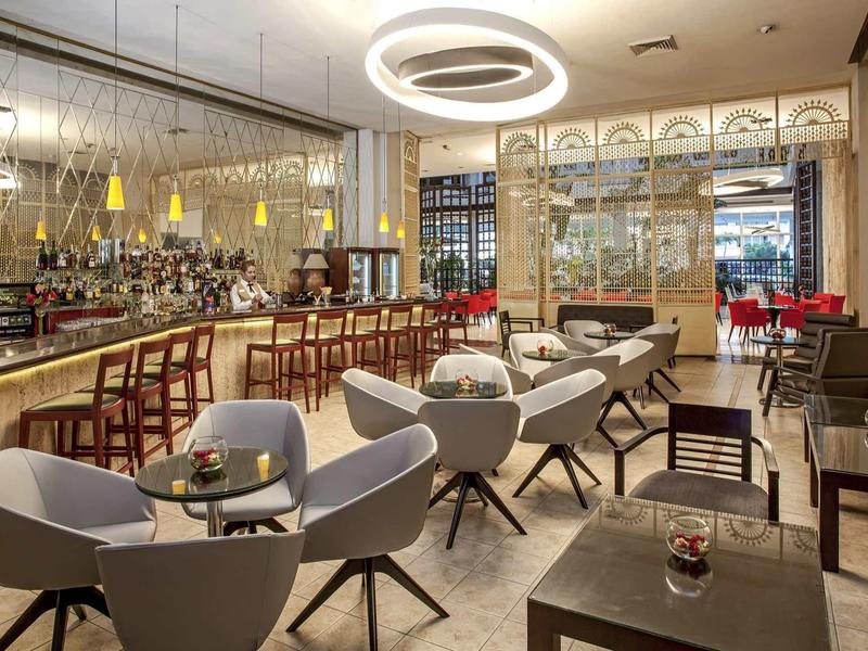 Moderner Restaurantraum mit grauen Sesseln, Holztischen, Bar und runden Deckenlampen.