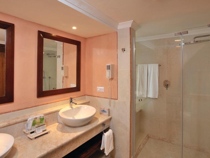 Moderner Badezimmer mit Doppelwaschbecken, großen Spiegeln, Marmorarbeitsplatte und Glastür zur Dusche.