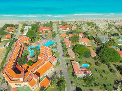 Luftaufnahme eines Strandhotels mit Pools, roten Dächern und angrenzendem Strand.