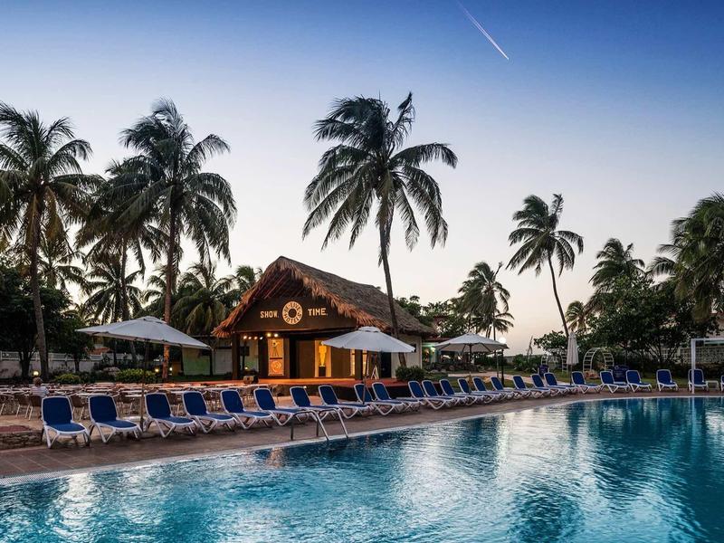 Ein einladender Pool mit blauen Liegestühlen und Palmen im Hintergrund bei Sonnenuntergang.