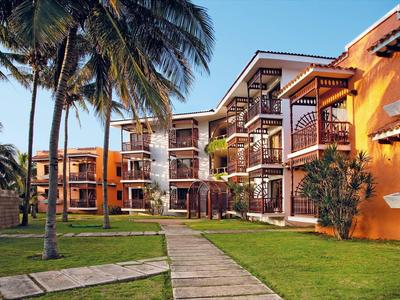 Mehrstöckige orangefarbene Gebäude mit Balkonen, umgeben von grünen Rasenflächen und hohen Palmen.
