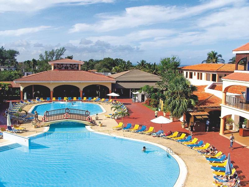 Grande piscina dell'hotel con ponte, ombrelloni e lettini sotto il cielo azzurro.