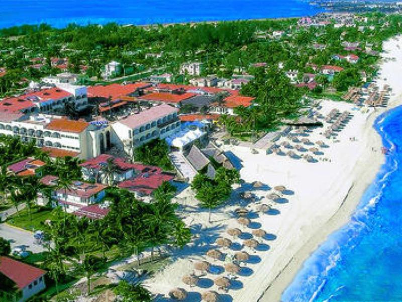 Complesso alberghiero con giardini di palme e ombrelloni su spiaggia di sabbia bianca vicino al mare blu