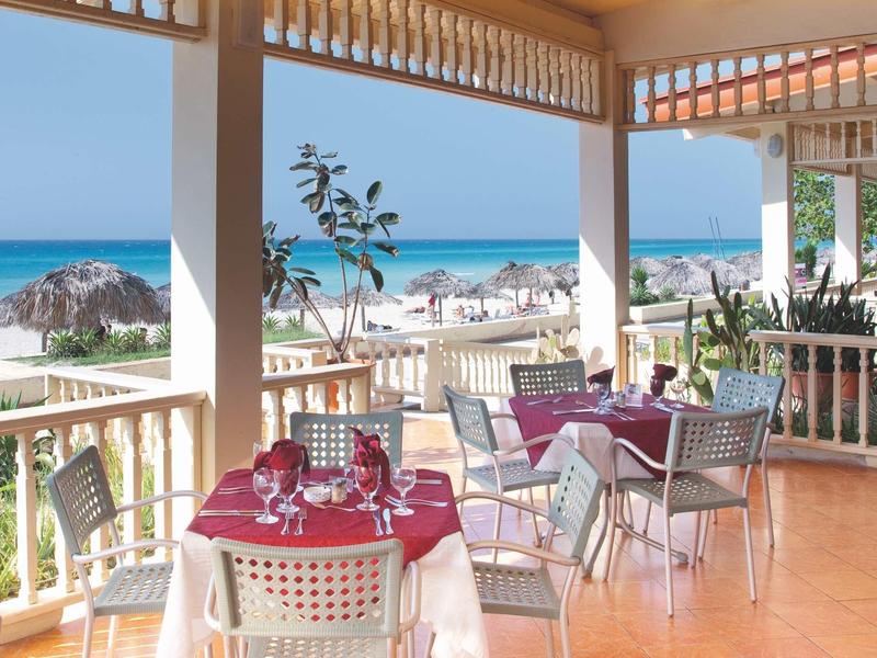 Terrazza con tavoli apparecchiati con vista sulla spiaggia e sul mare in una giornata di sole.