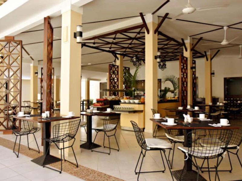 Area ristorante hotel aperta con tavoli rotondi e sedie in filo sotto un tetto.