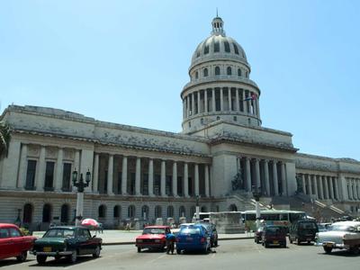 Large neoclassical building with dome and cars on the street in front
