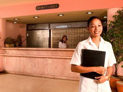 Receptionist stands in front of hotel lobby holding a folder.