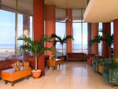 Bright hotel lobby with large windows, plants, and cozy seating areas with couches and tables.