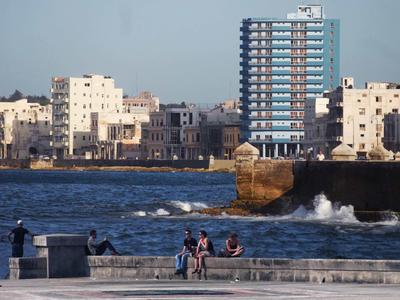 People sit by the water with modern and old architecture in the background.