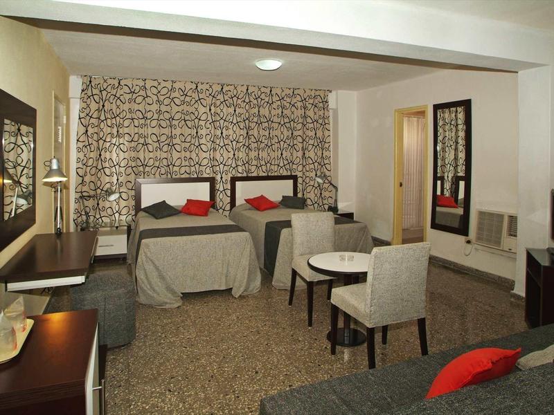 Hotel room with two single beds, seating area, desk, and carpeted floor.