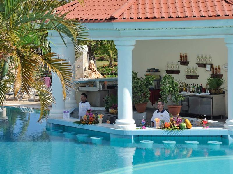 Piscina con bar integrato e colonne bianche, circondata da vegetazione tropicale.