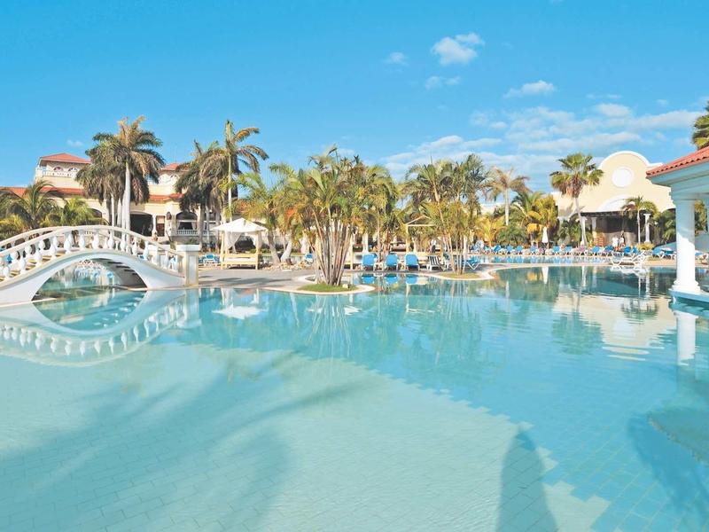Piscina di un hotel con ponte, palme e cielo sereno.