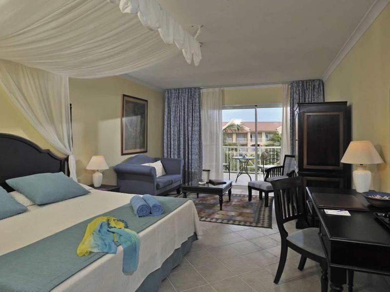 Camera d'albergo elegante con letto matrimoniale, scrivania, poltrone e vista giardino.