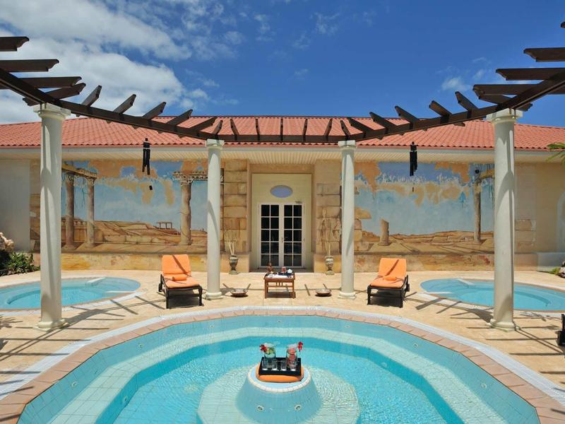 Villa con piscina rotonda blu, lettini arancioni e muro decorato sotto cielo parzialmente nuvoloso.