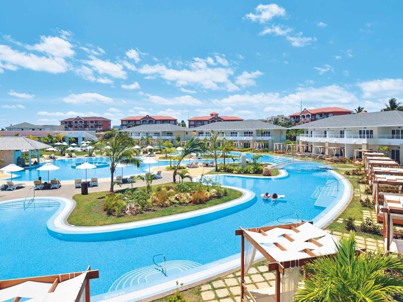 Piscina a forma di laguna circondata da lettini e edifici dell'hotel sotto un cielo blu.