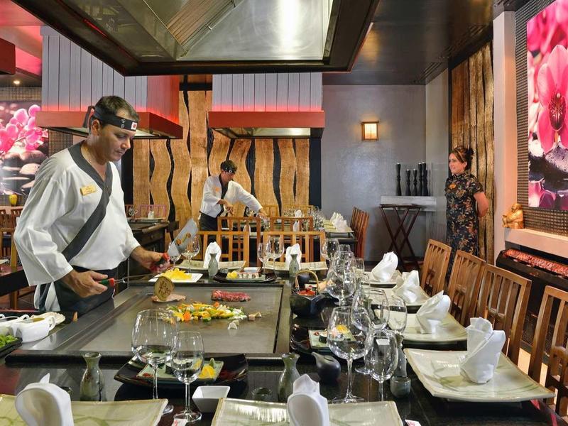 Ristorante elegante con chef che cucina su piastra centrale attorno a un tavolo apparecchiato.