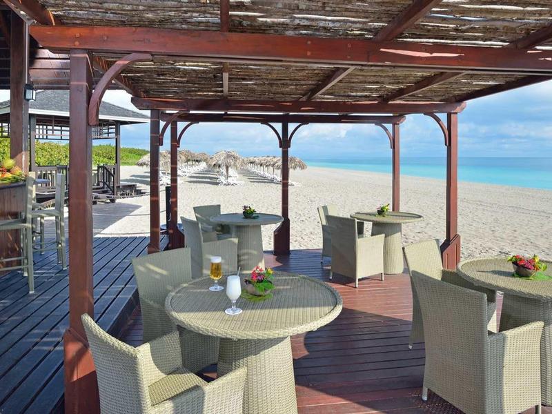 Terrazza coperta con tavoli rotondi e vista sulla spiaggia e il mare calmo.