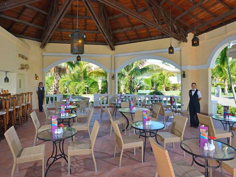 Terrazza di ristorante con tavoli, sedie e vista su giardino tropicale.